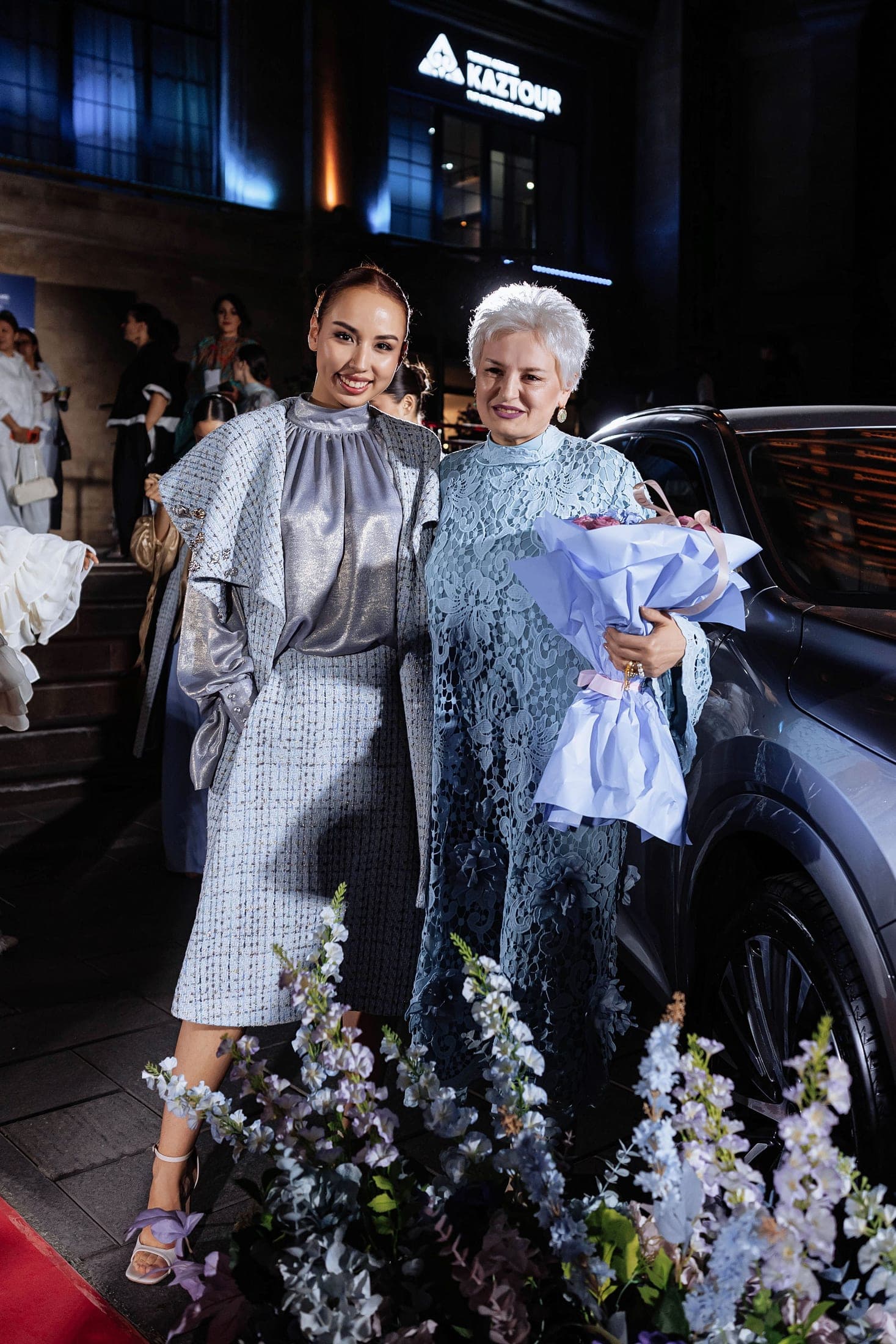 Models and the designer posing between two Lexus cars outside the venue at night