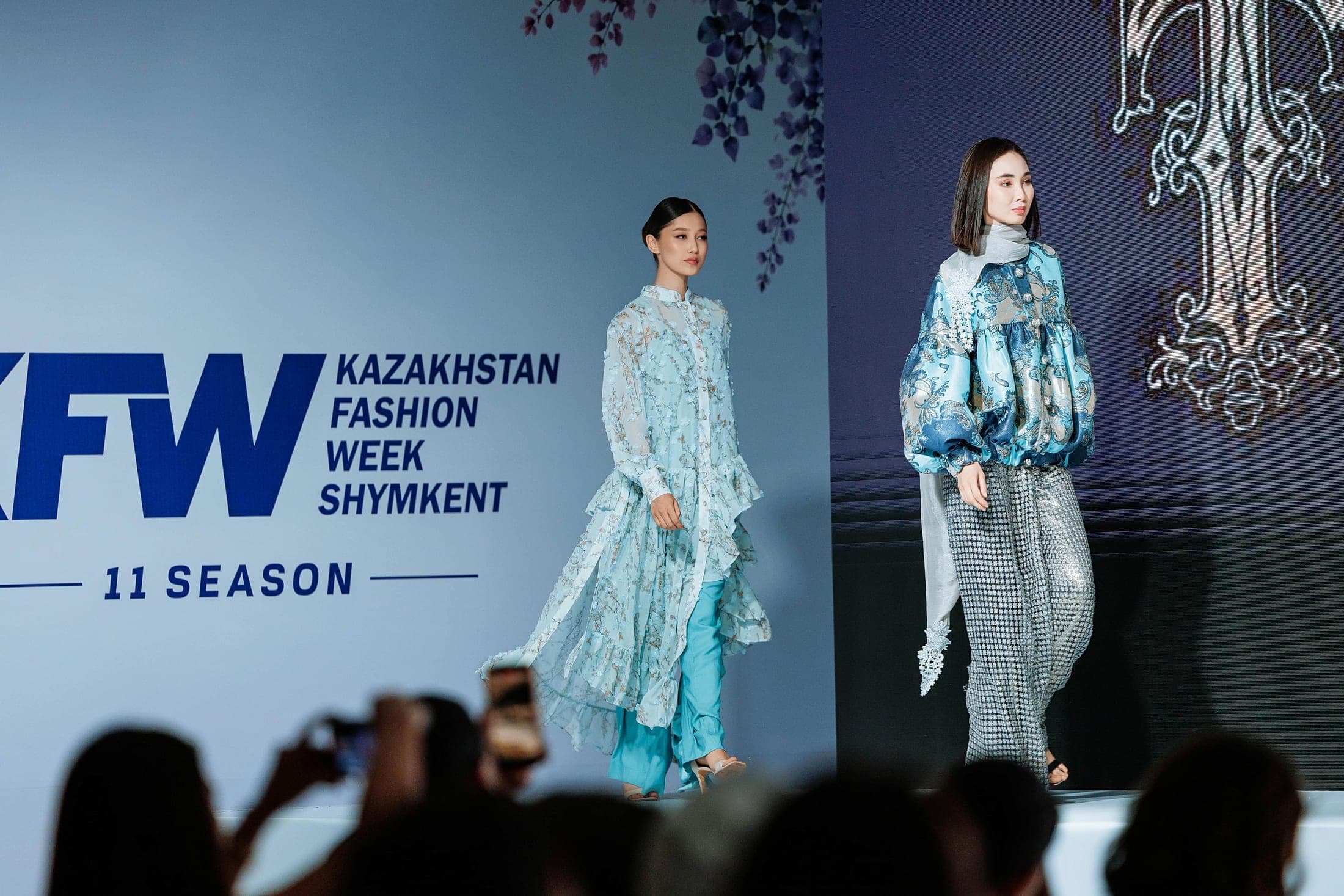 Two models on the runway in a metallic silver blouse with blue tweed skirt and a blush look with a lace headscarf