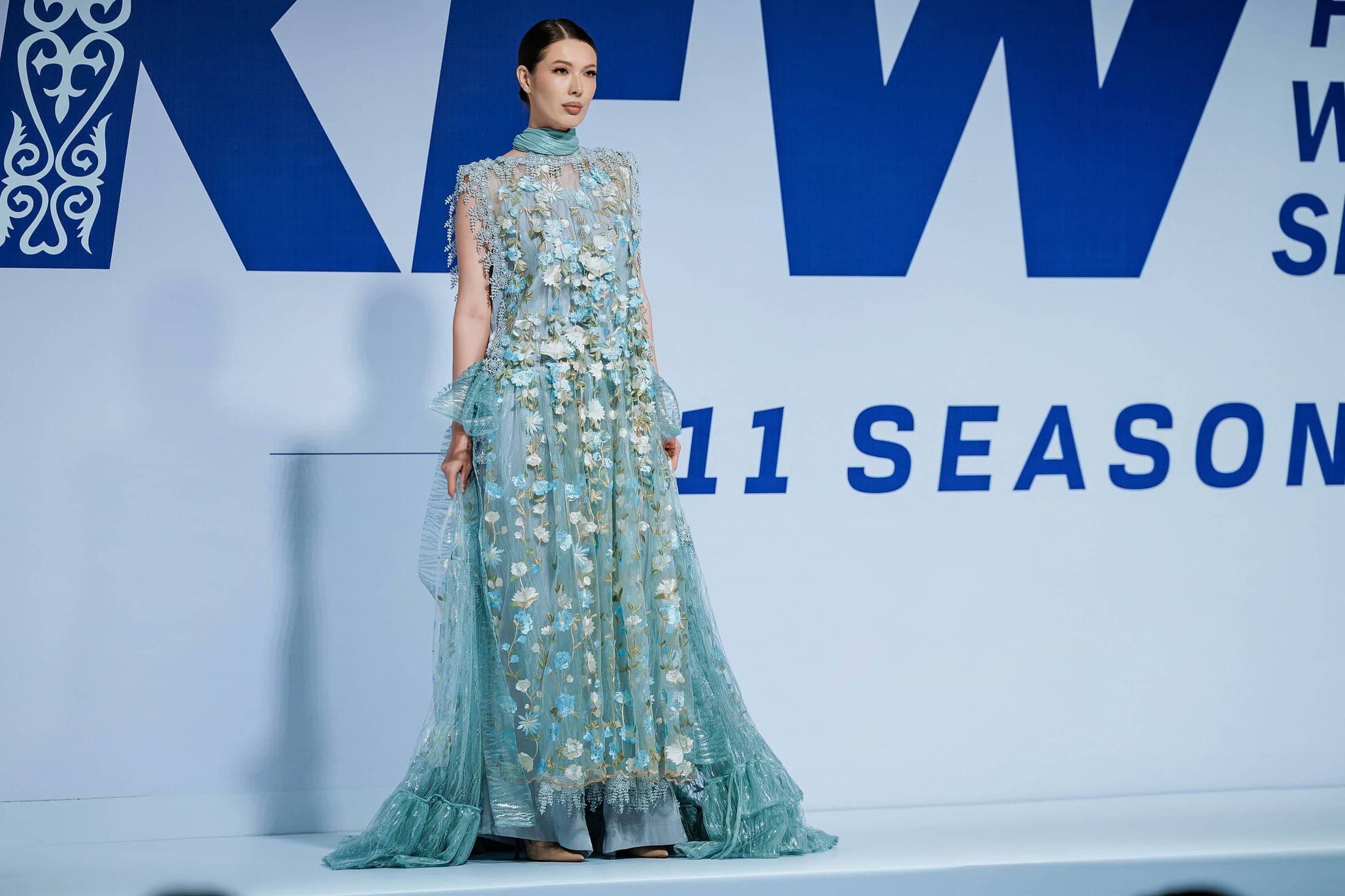 The designer in blue lace with a model in a silver blouse and tweed skirt, flowers and a Lexus behind them