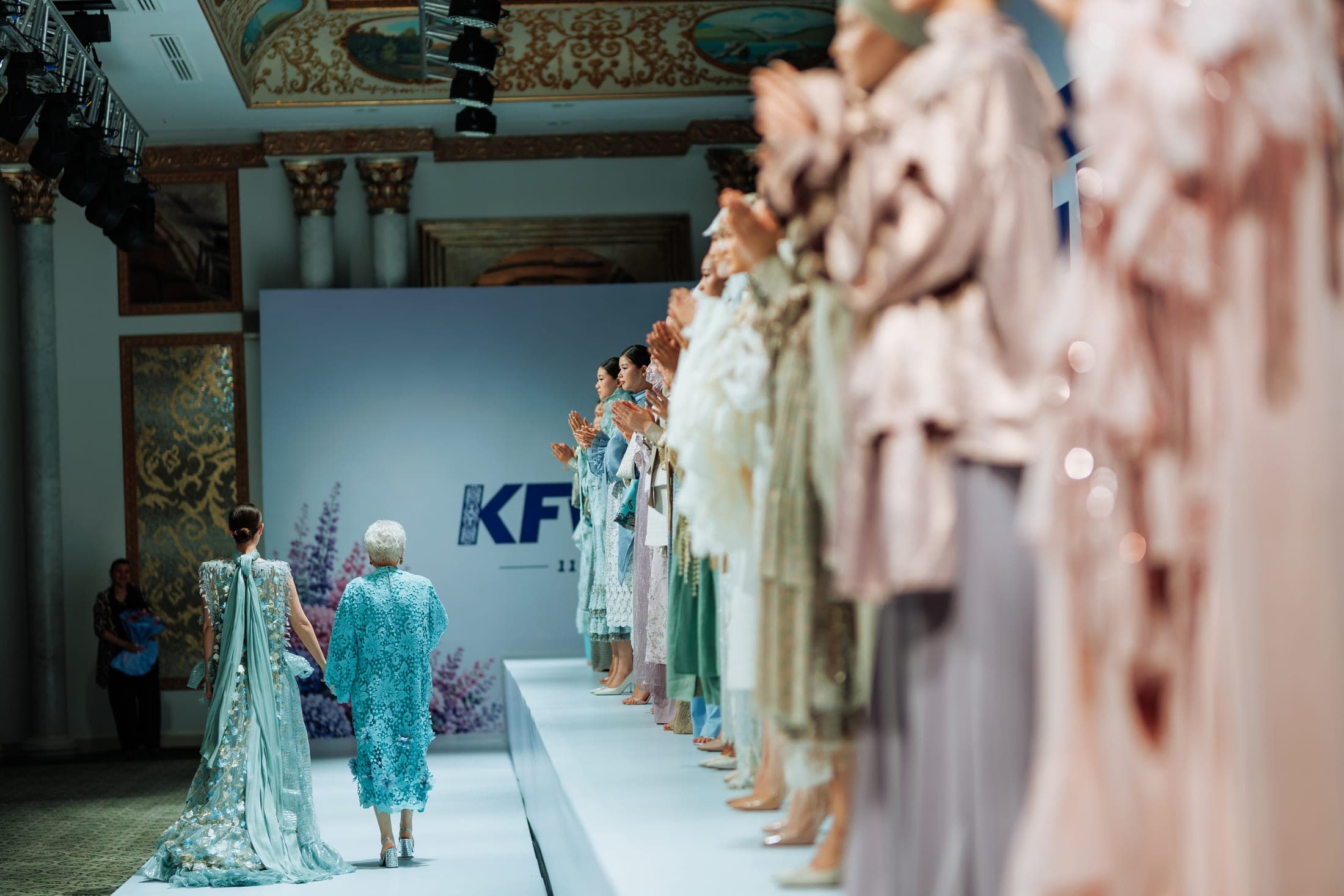The designer and a model in matching turquoise lace and floral-embroidered gowns walking the runway hand in hand