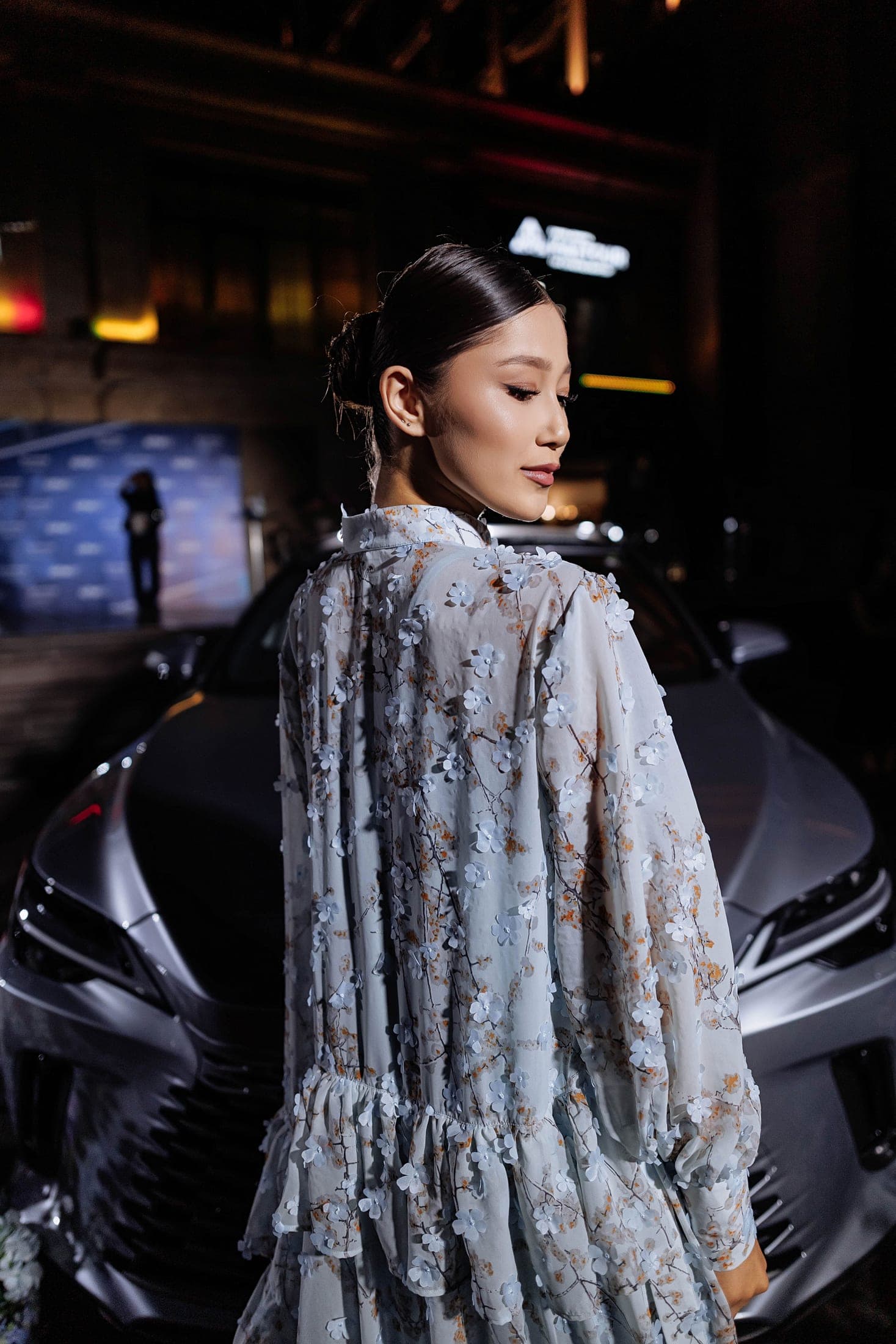 Model glancing over her shoulder in a sheer blossom-appliqué dress, beside a car at night